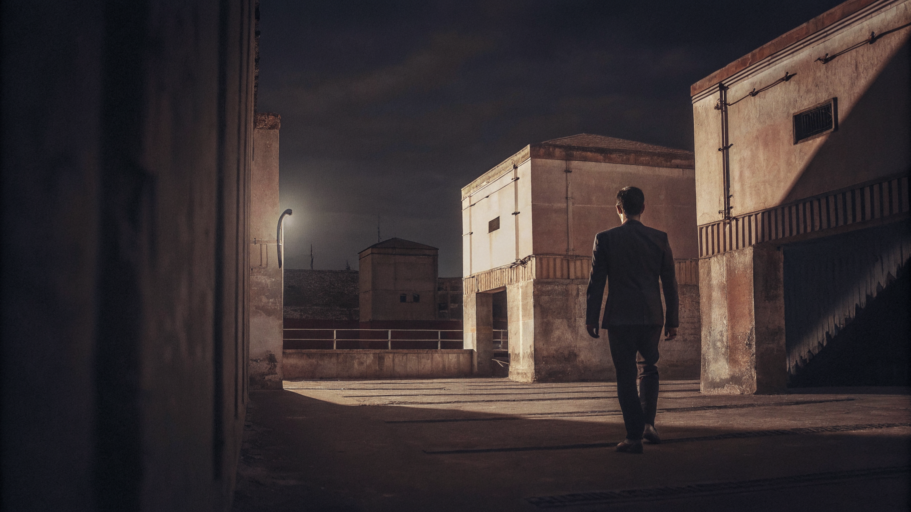 Editorial photograph of a lone figure crossing open ground toward distant structures