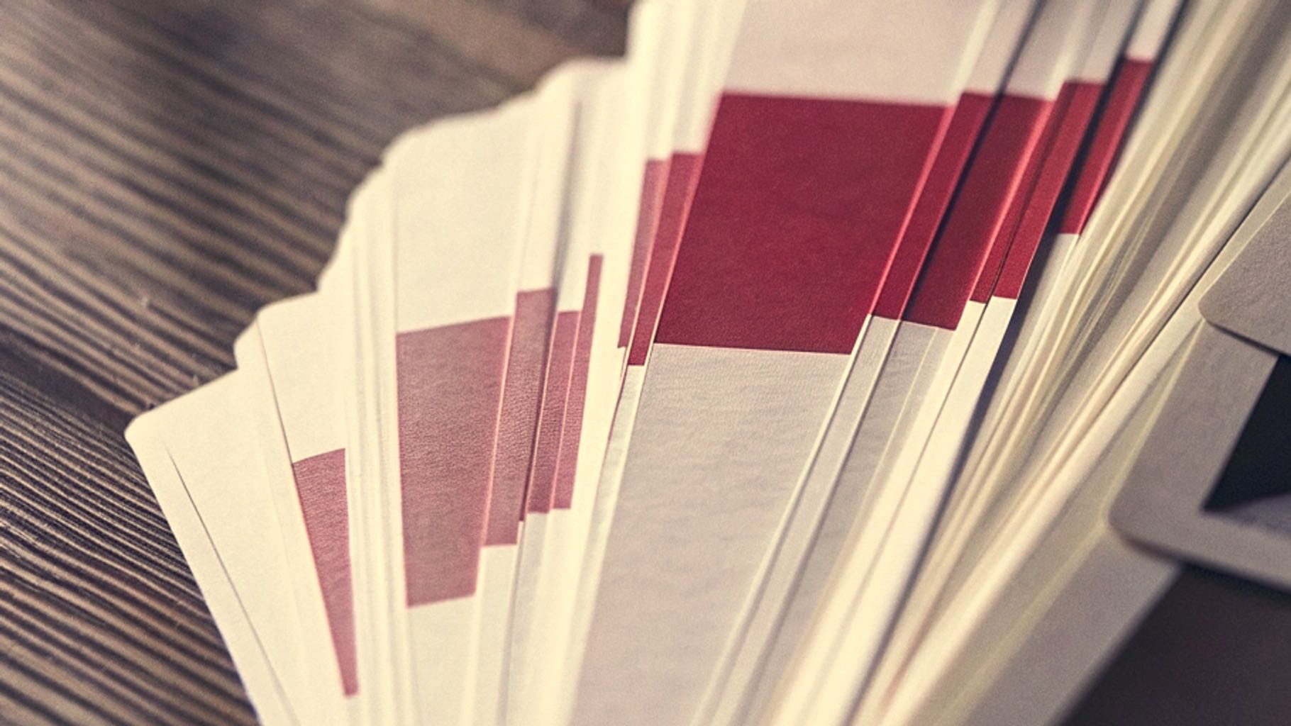 A fanned pile of the same printed card, each copy's red band sitting at a slightly different height and in a slightly different shade